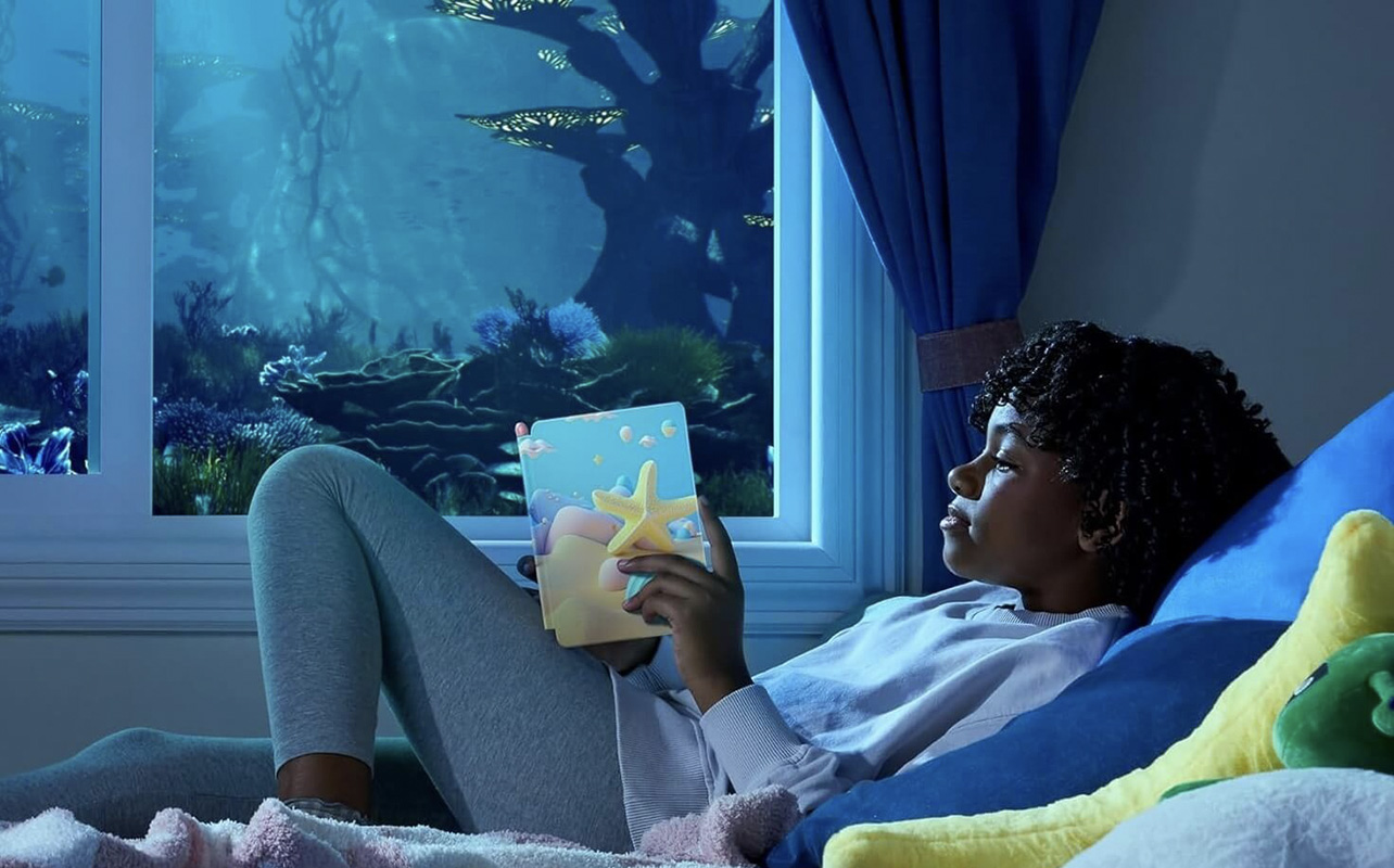 A kid lying in bed reading on an Amazon Kindle Kids ereader.