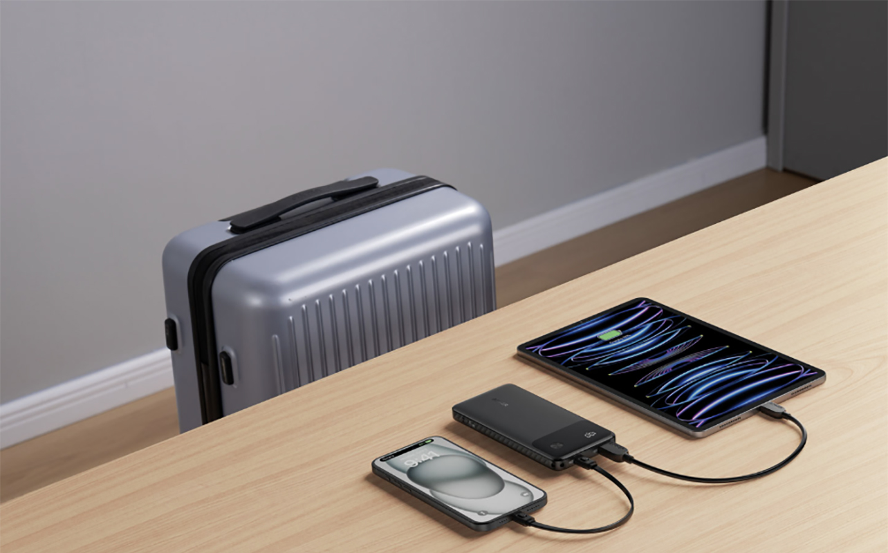 Anker portable charging charging a phone and tablet on a tablet beside a suitcase.