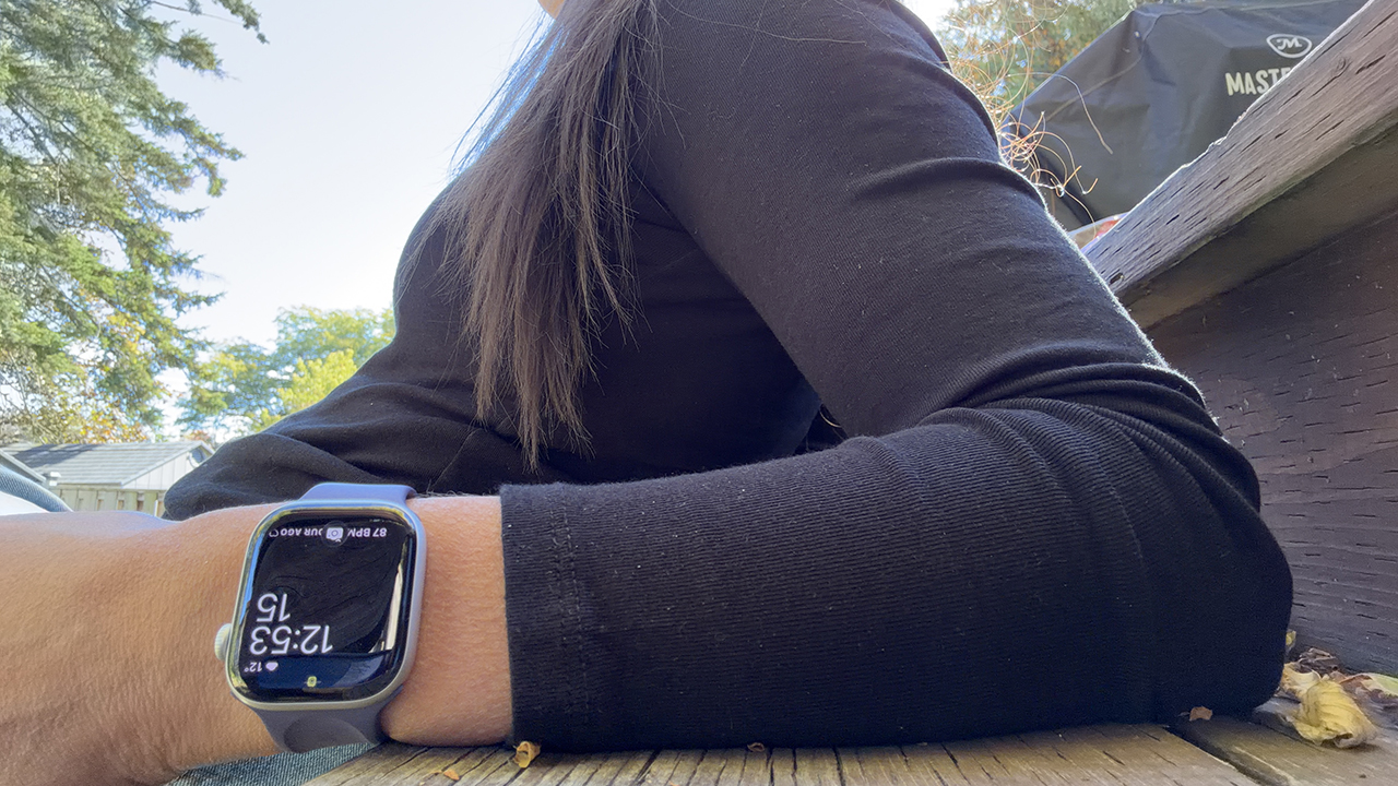 A woman sitting with an Apple Watch Series 11 on her wrist.