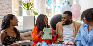 Smiling pregnant woman getting presents at baby shower. Happy mother to be receiving gifts from friends at baby shower party.