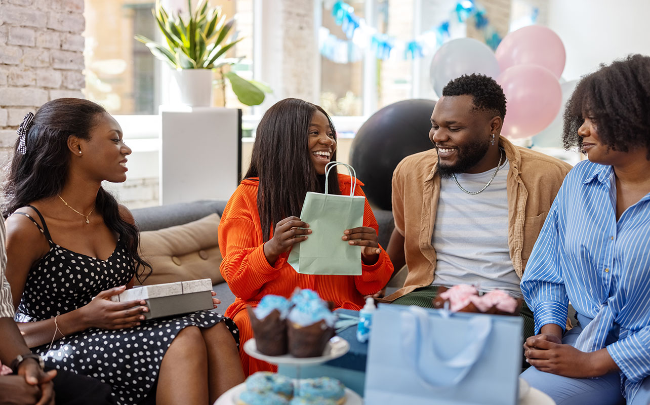 Smiling pregnant woman getting gifts for new parents at baby shower.  Happy mother to be receiving presents from friends at baby shower party.