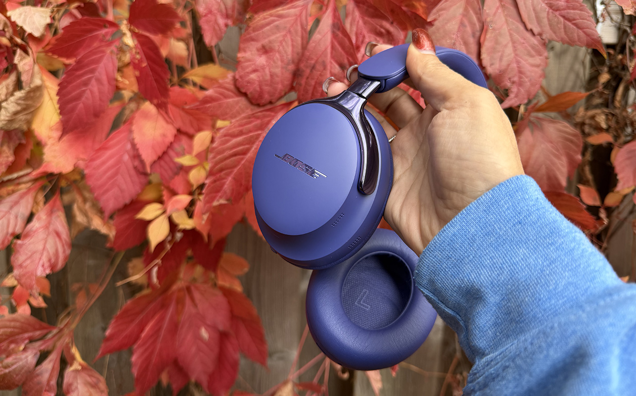 Bose QuietComfort Ultra 2nd Gen headphones held by hand in front of changing Fall leaves.