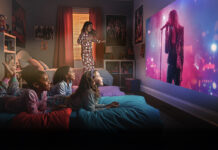 Two kids lying on a bed watching a movie on a projector screen using an Epson projector.