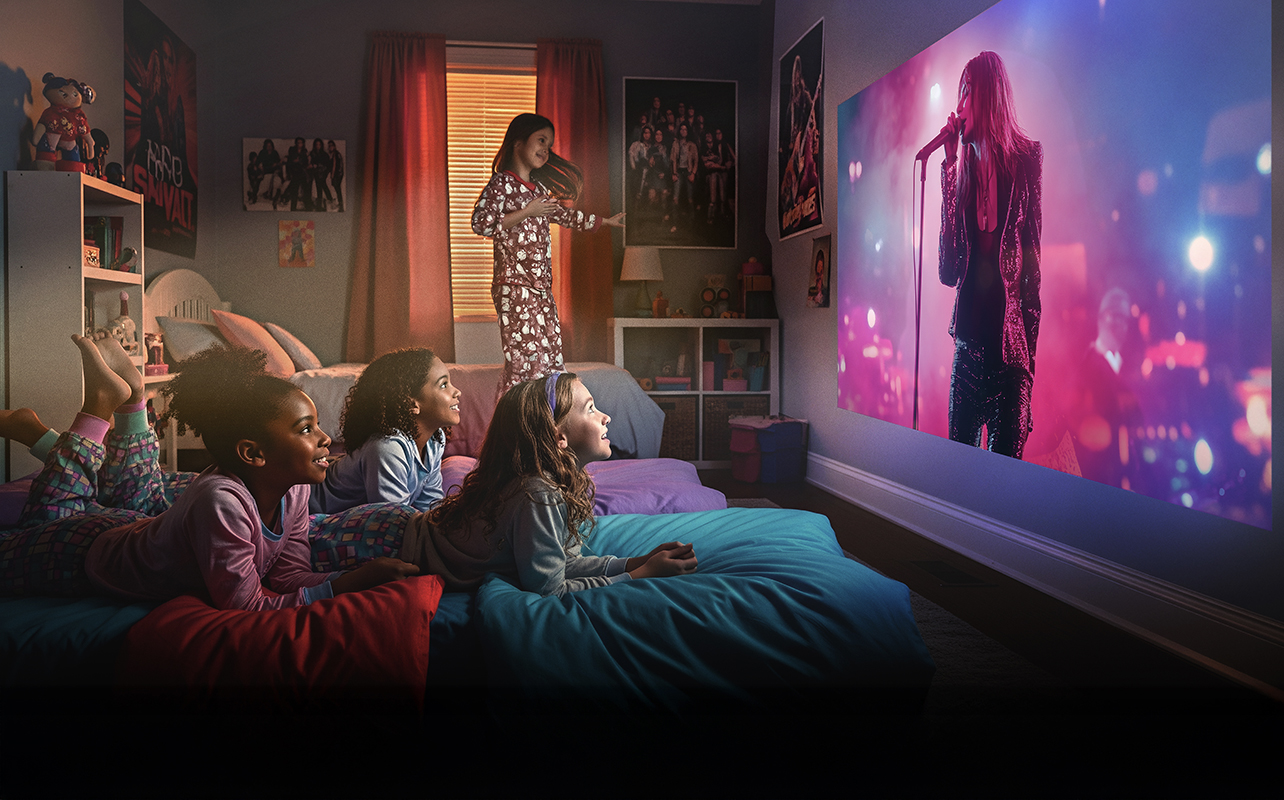 Two kids lying on a bed watching a movie on a projector screen using an Epson projector.