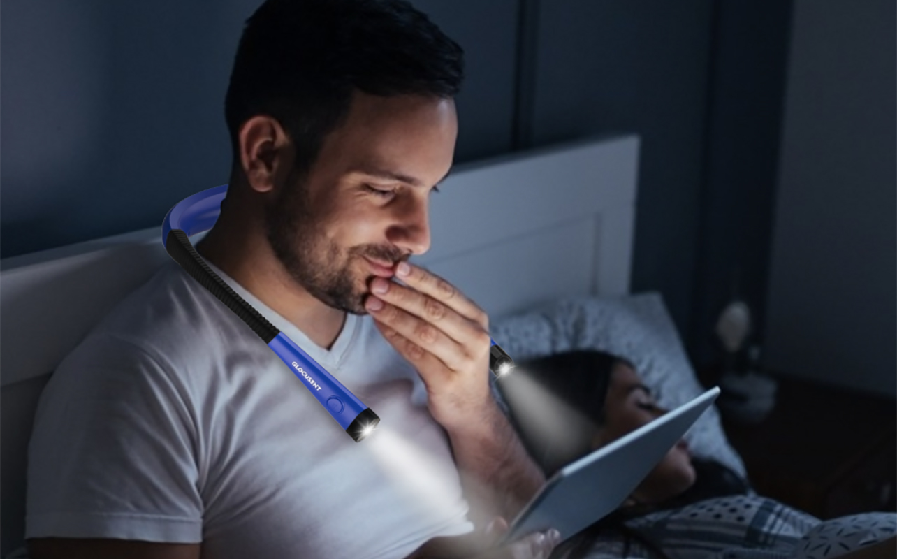 A man sitting up reading at night with a neck light.