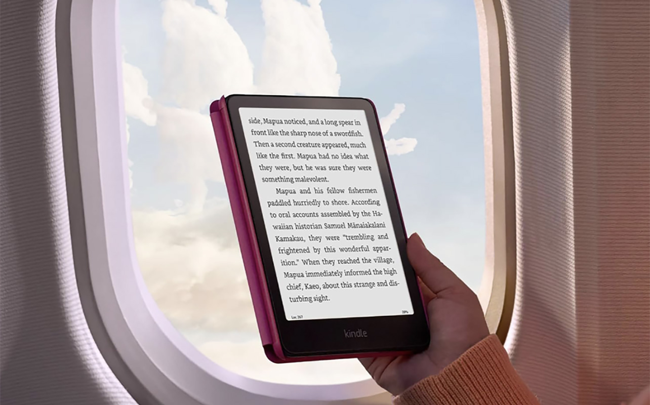 A hand holding a Kindle Paperwhite eReader in front of an airplane window.