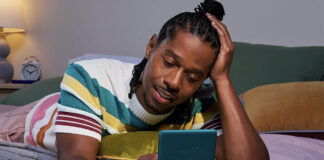 A man lying on a bed reading on a Kindle Paperwhite.