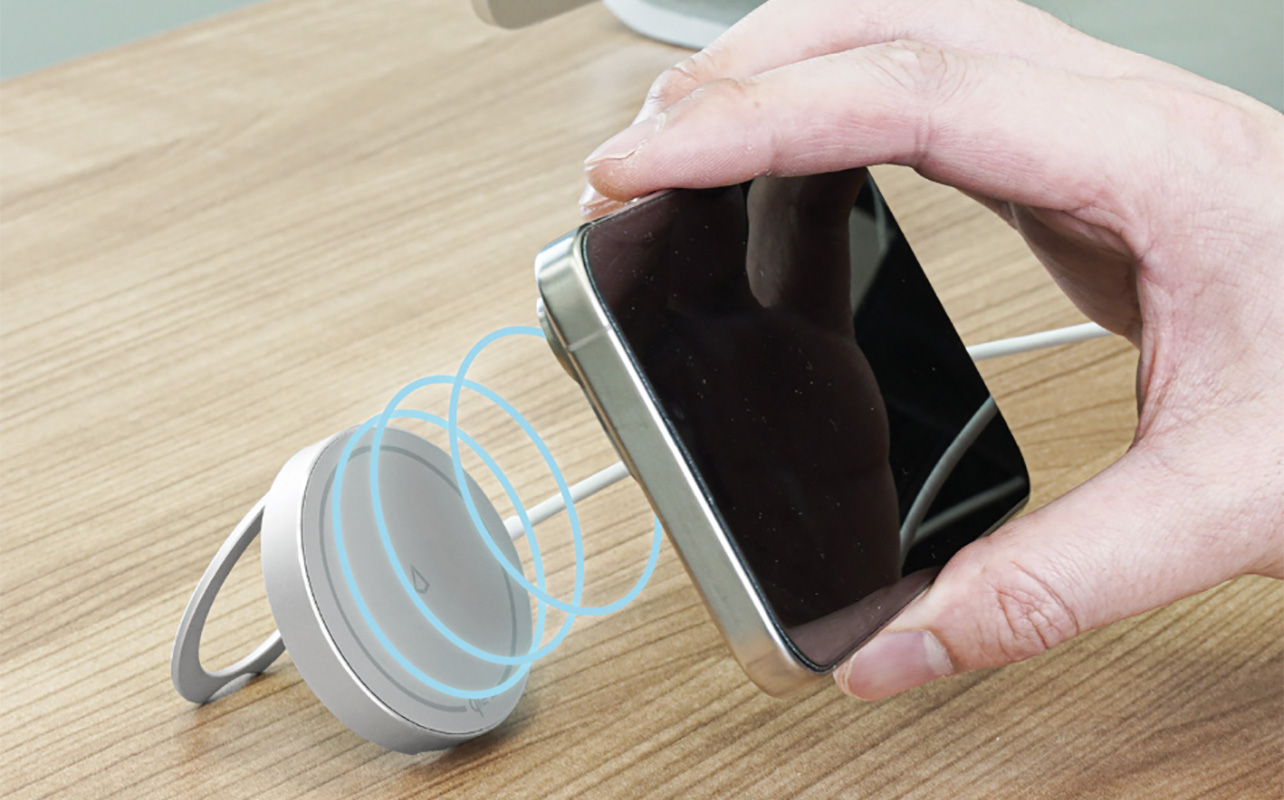 A hand placing a phone onto an LBT Qi2 wireless charger.