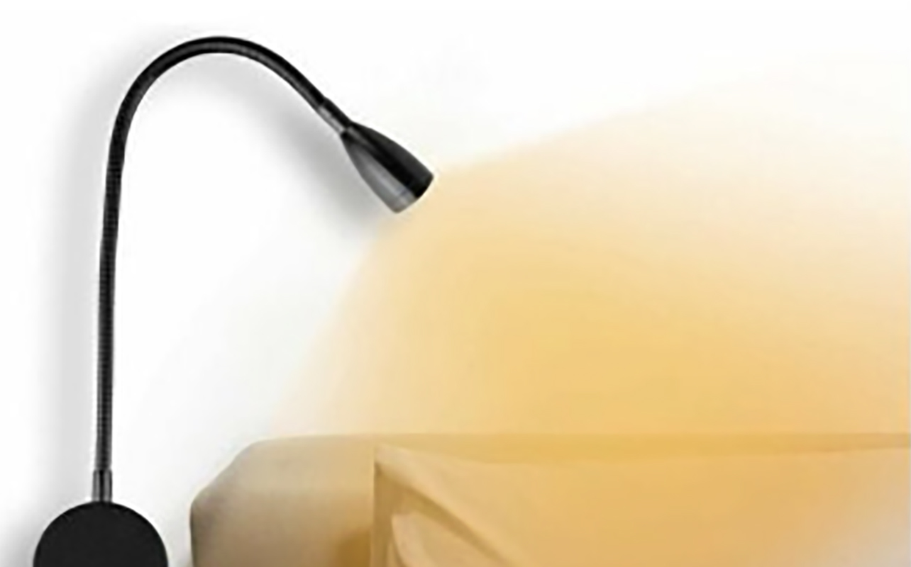A reading light mounted on the wall and shining on a bed.