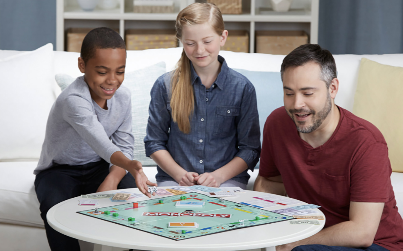 A man and two kids playing Monopoly.