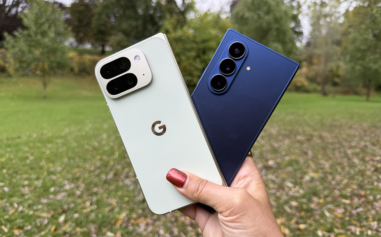 A hand holding the Google Pixel 10 Pro Fold and Samsung Galaxy Z Fold 7 outside.