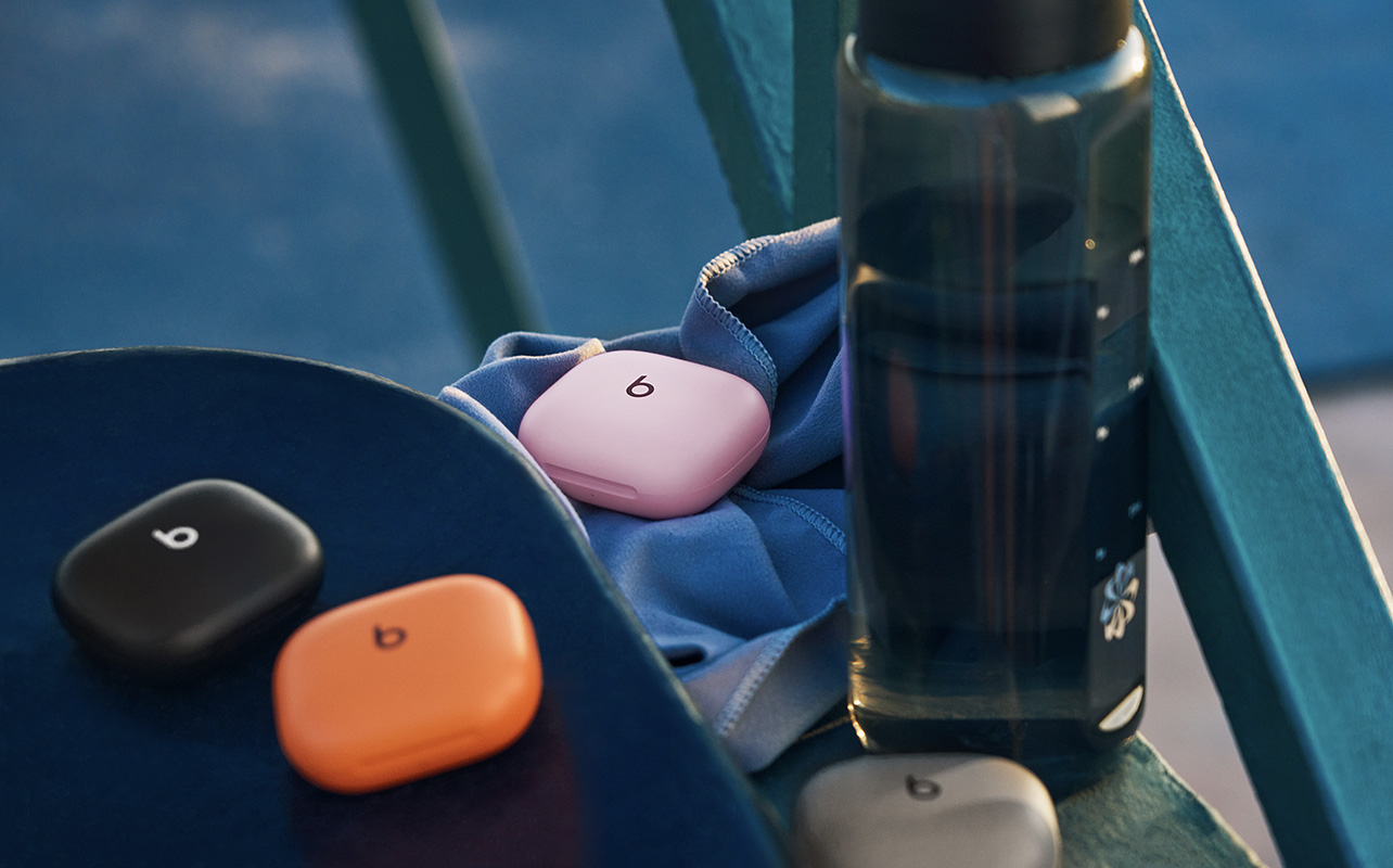 All four colours of the Powerbeats Fit earbuds in their cases beside a water bottle.