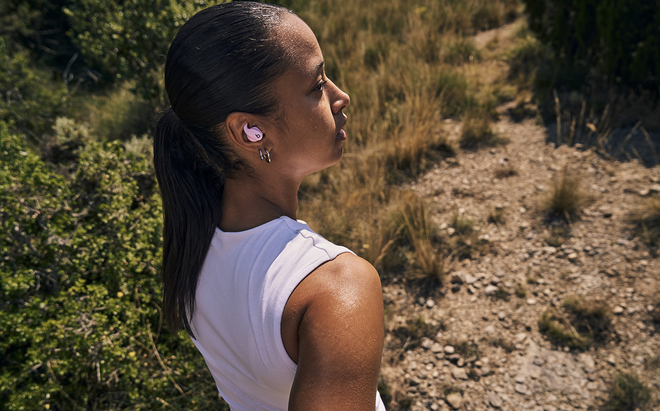 A woman walking on a trail wearing the Powerbeats Fit earbuds.