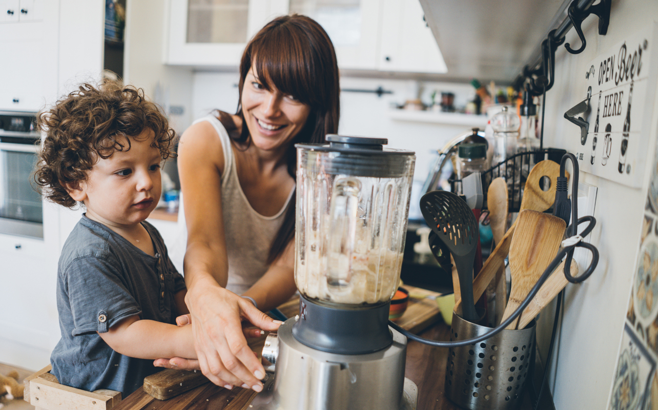 Mom with her toddler boy prepares healthy food together using blender