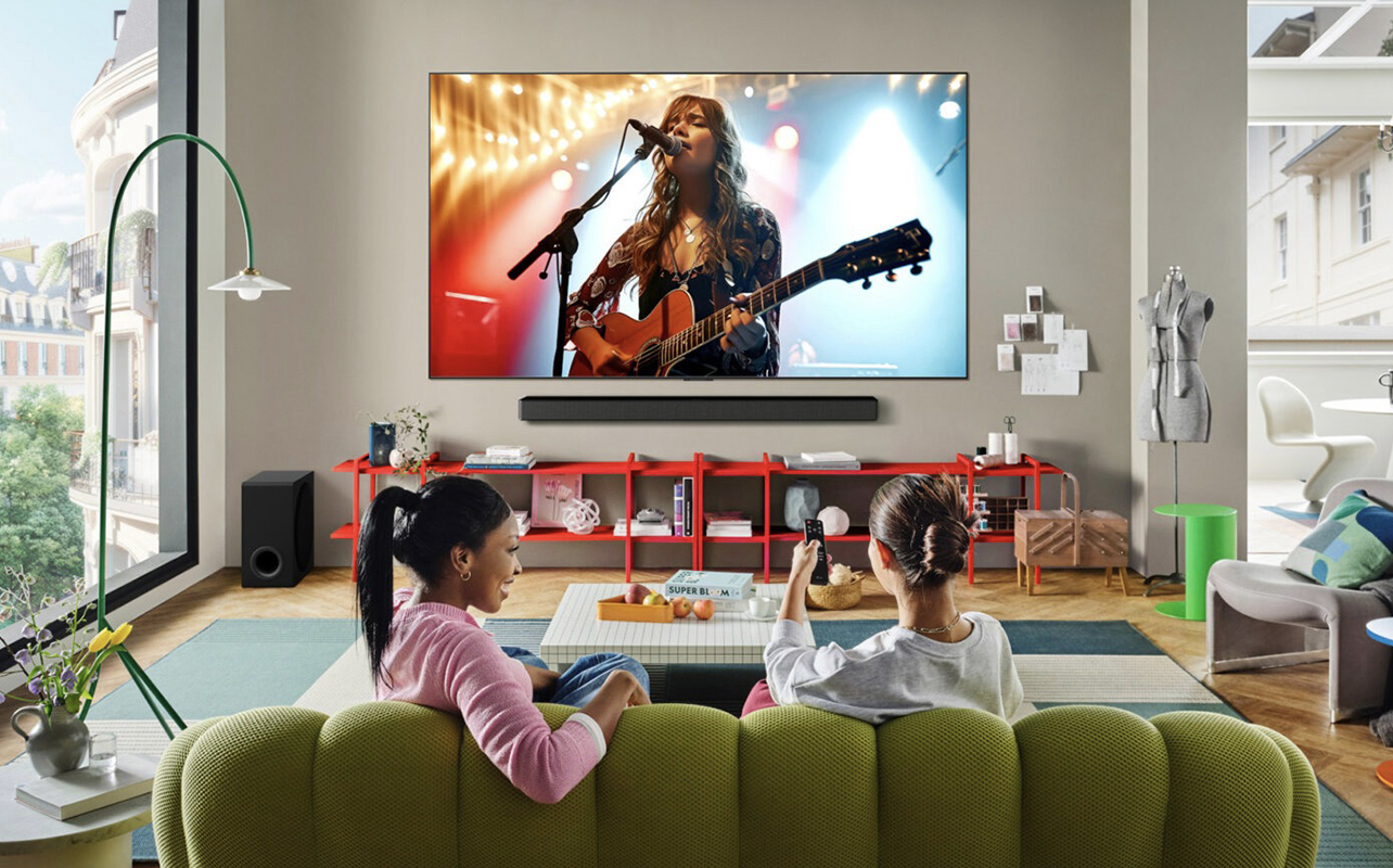 Two women watching a concert on an LG C5 OLED TV in a living room.