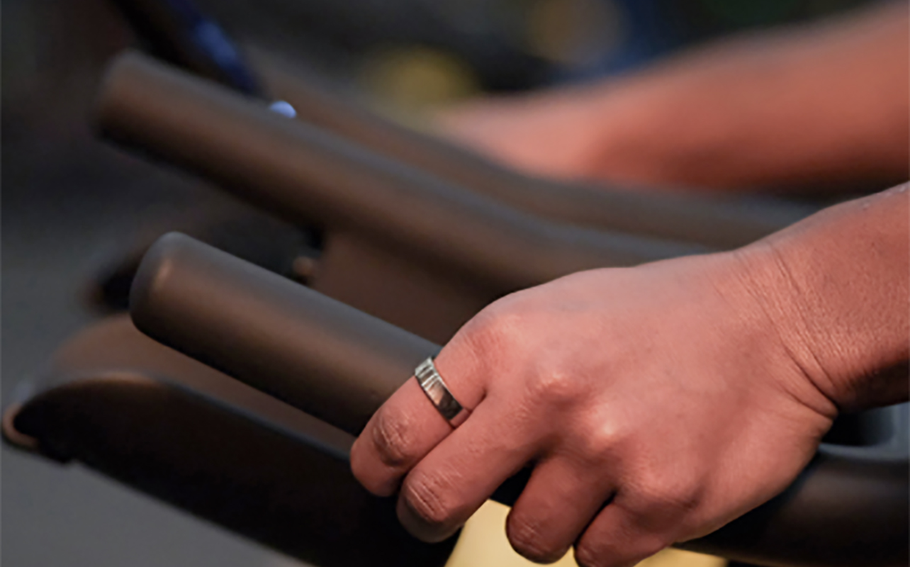 A hand on the handles of a stationary bike wearing the Ringconn Gen 2 Air smart ring.