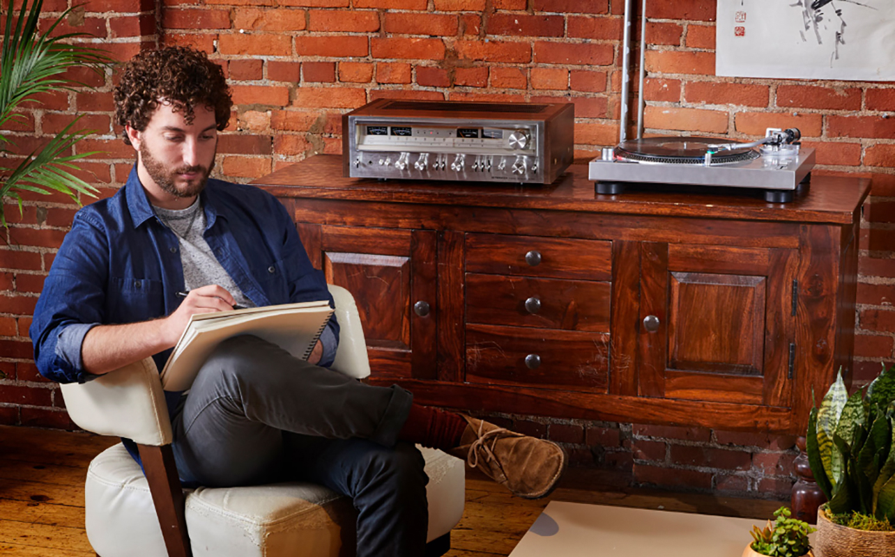A man sitting beside an Audio Technica AP-LP120XUSB turntable.