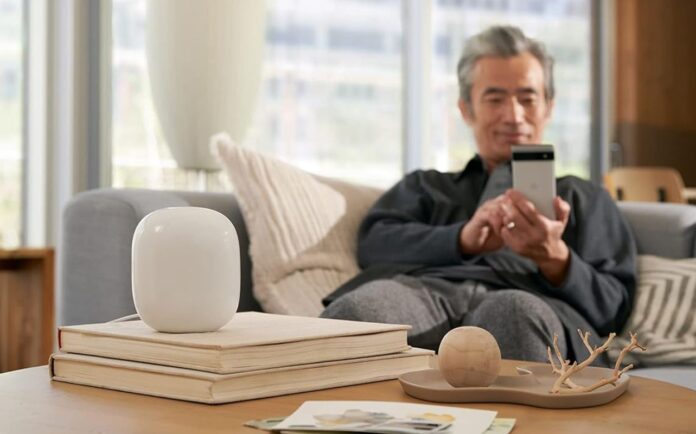 A man sitting on the couch with a Nest Wi-Fi router in front of him.