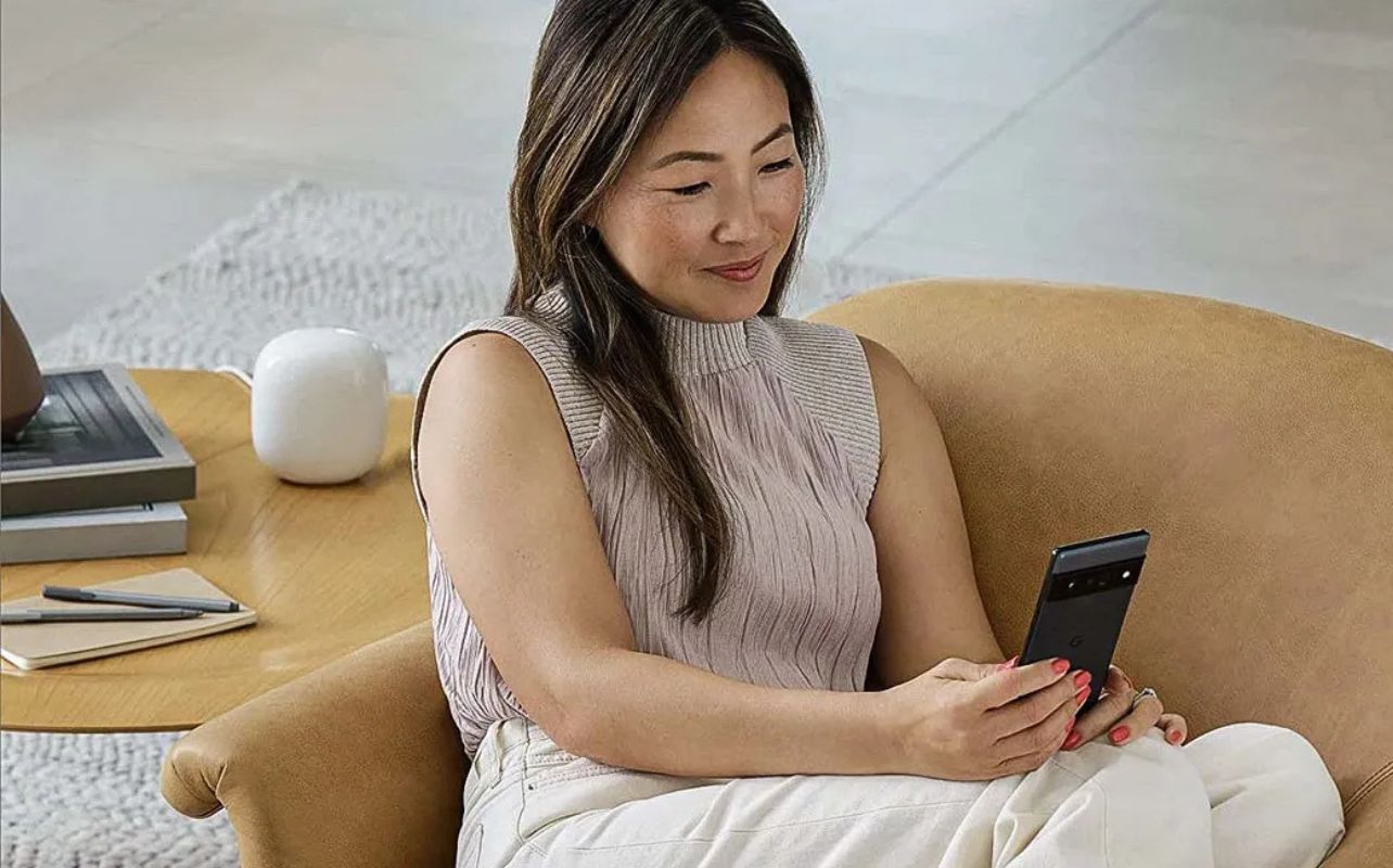 A person enjoys internet on their phone next to the Google Nest hub.
