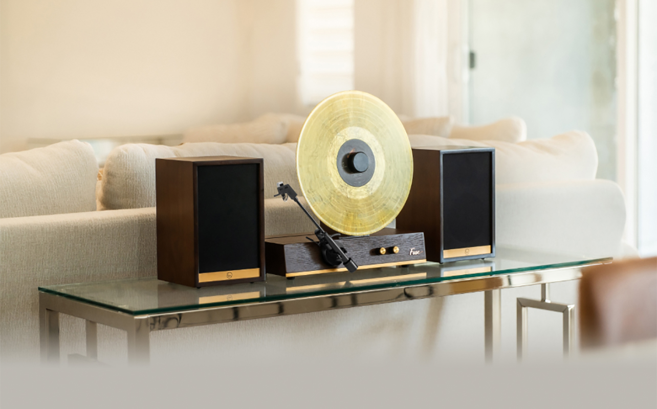 A Fuse Gold vertical record player with speakers on a table behind a couch.