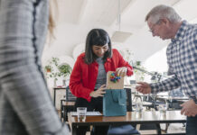 A woman receiving last-minute gifts in a bag from her colleagues and celebrating at the office after a recent success.