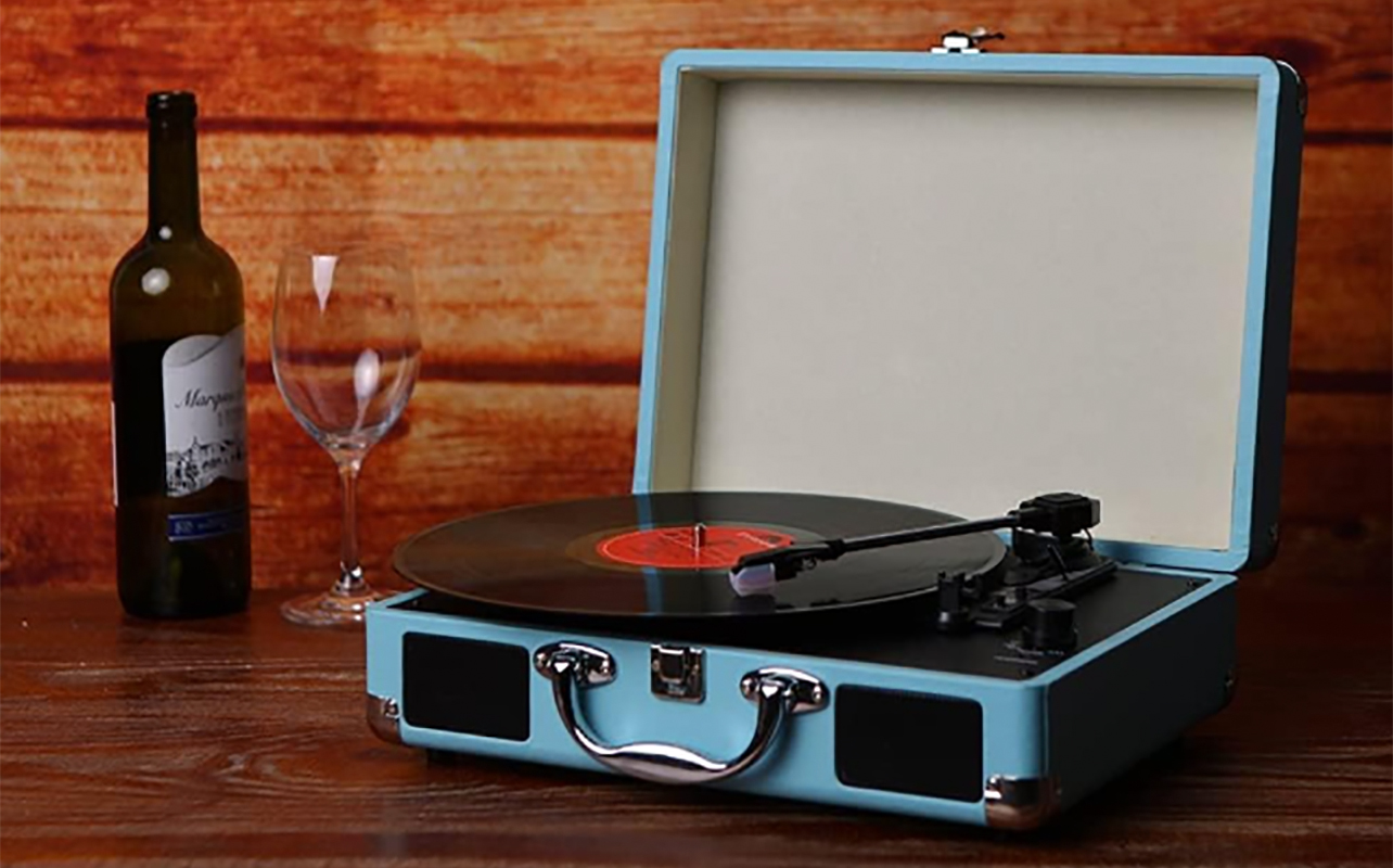 A vintage portable record player suitcase design with a bottle of wine beside it.