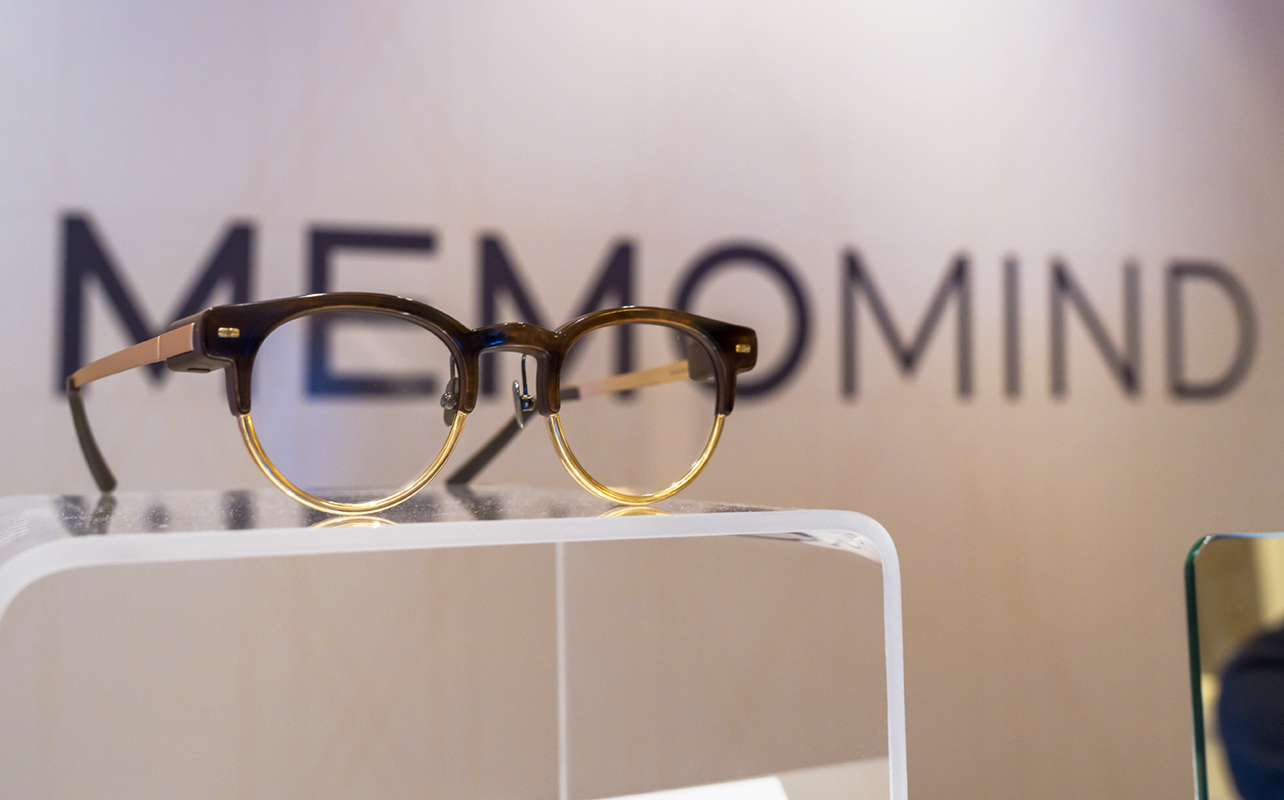 MemoMind smart glasses on top of display in front of logo at CES 2026.