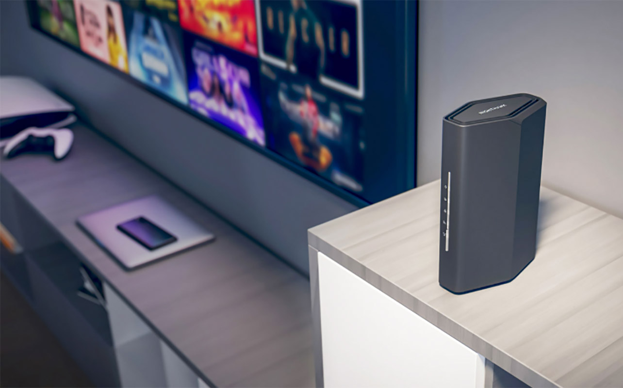 A Netgear Nighthawk BE3600 router beside a monitor on a desk.