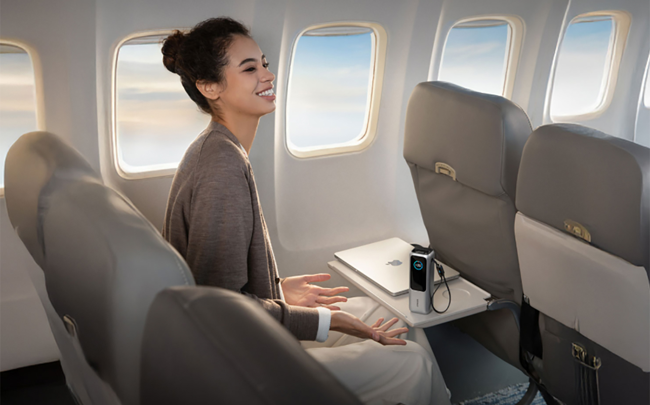 A woman sitting on a plane with the tray table option and her laptop and an Anker Prime 25,000 mAh power bank connected.