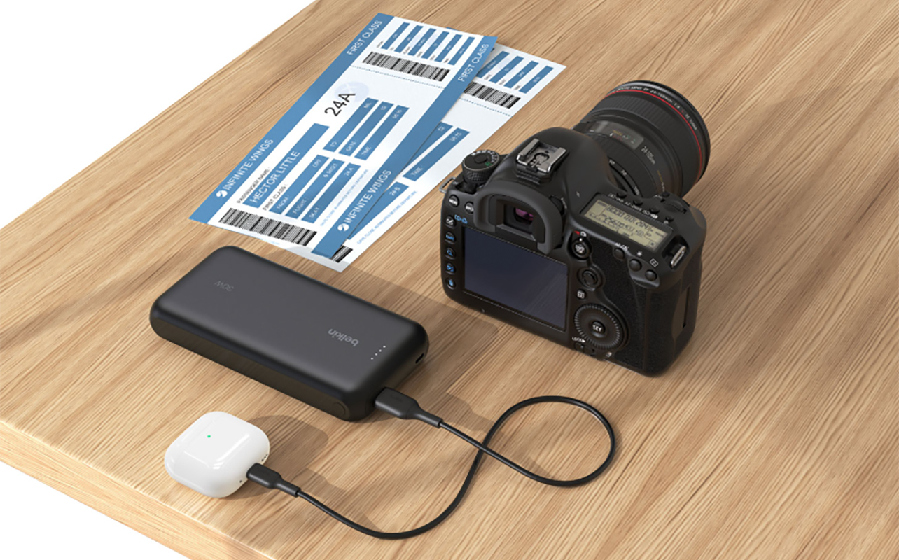 A Belkin BoostCharge power bank on a tablet connected to a DSLR camera and earbuds.