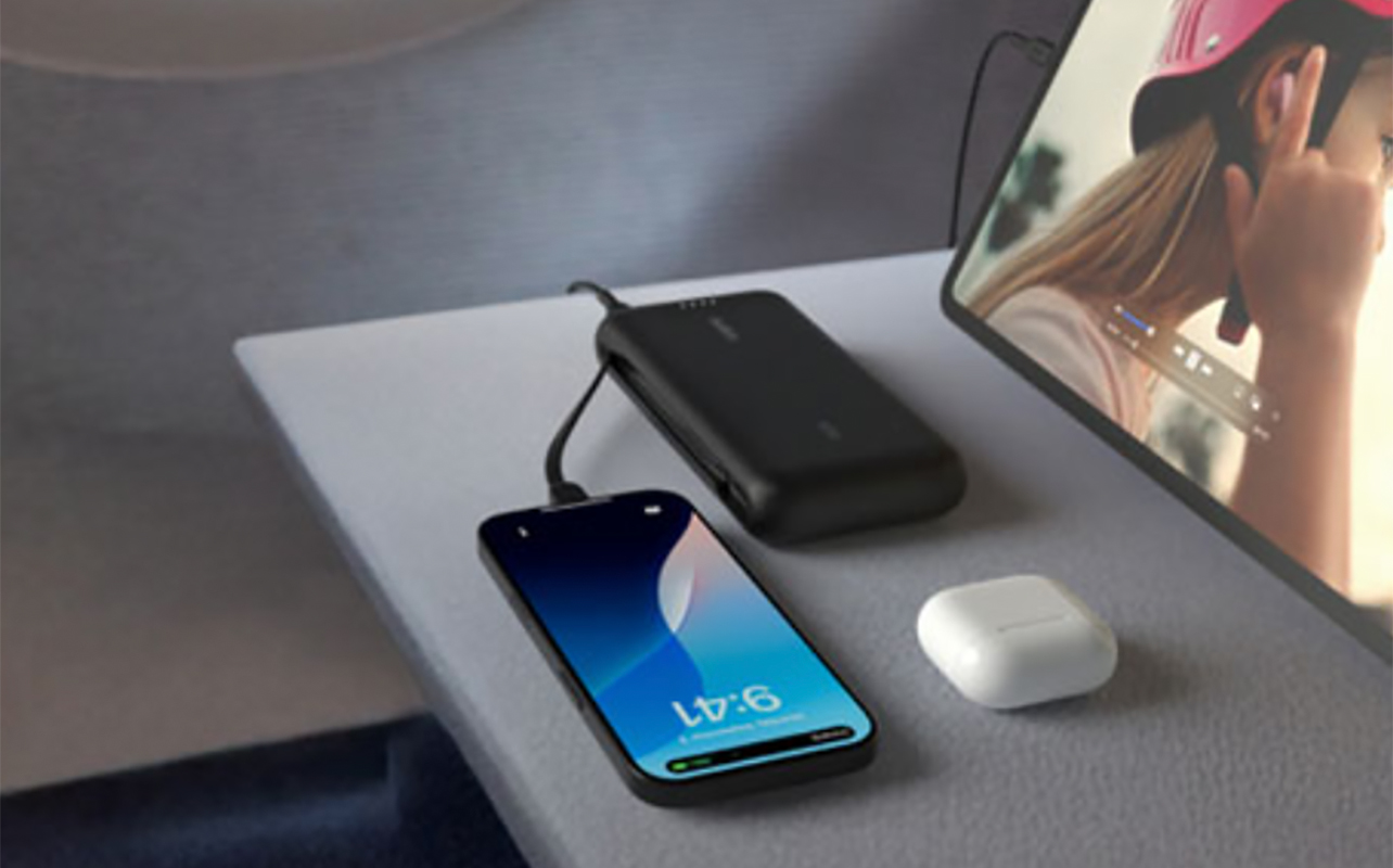 A Belkin BoostCharge 20,000mAh power bank on a table with a phone and earbuds.