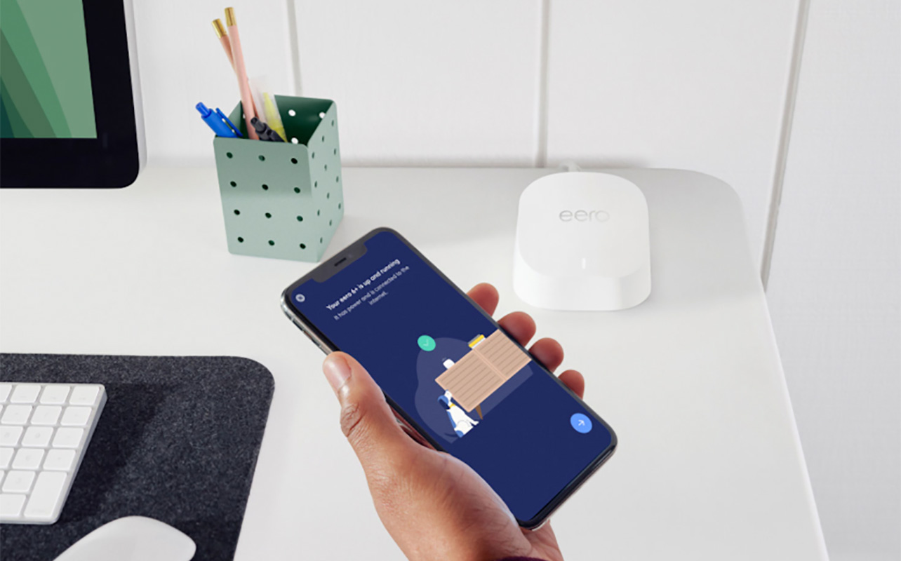 A hand holding a phone with the eero 6 mesh router app.