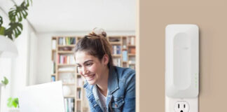 A woman on her laptop on the left and a Netgear AX3000 range extender mounted on the wall on the right.