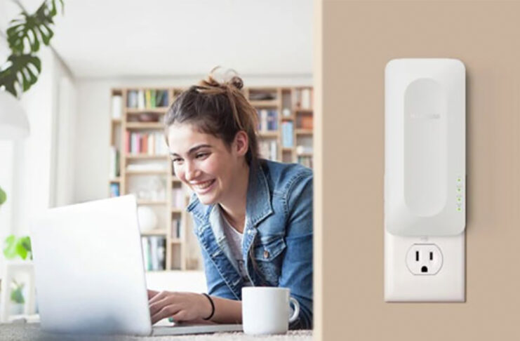 A woman on her laptop on the left and a Netgear AX3000 range extender mounted on the wall on the right.