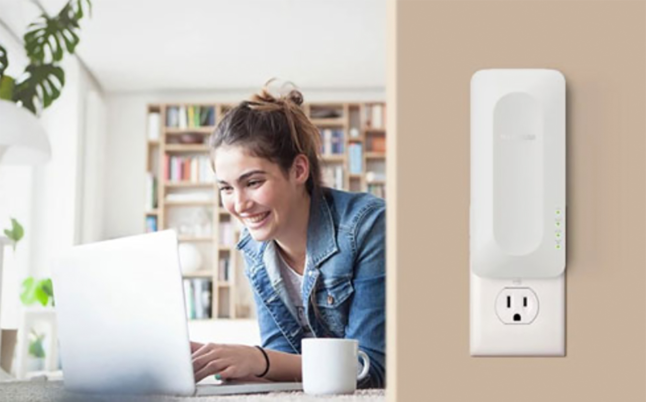 A woman on her laptop on the left and a Netgear AX3000 range extender mounted on the wall on the right.