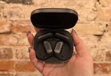 The Shokz OpenFit Pro earbuds in their case against a brick wall.