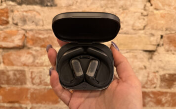 Shokz OpenFit Pro are open-ear earbuds with noise reduction that works The Shokz OpenFit Pro earbuds in their case against a brick wall.