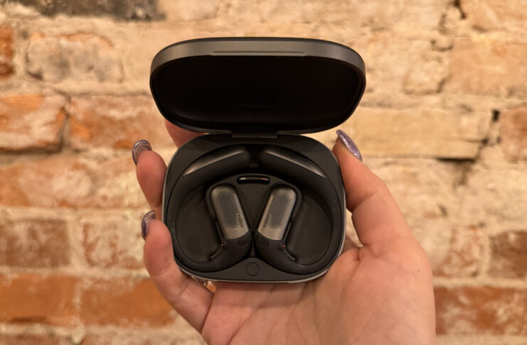 Shokz OpenFit Pro are open-ear earbuds with noise reduction that works The Shokz OpenFit Pro earbuds in their case against a brick wall.