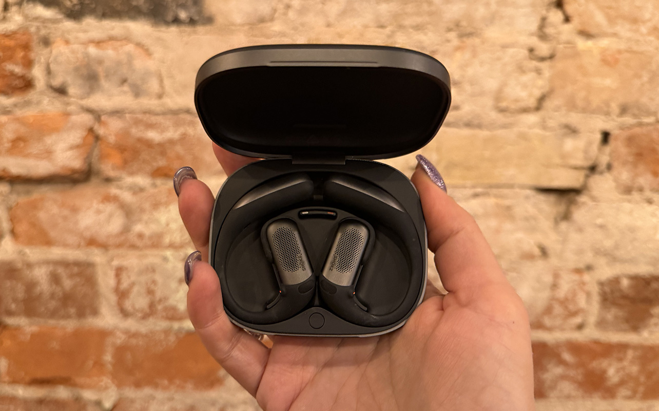 The Shokz OpenFit Pro earbuds in their case against a brick wall.