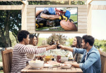 Are outdoor TVs worth it and should you get one? Four friends on a patio clinking glasses, a Neptune Full Sun outdoor TV behind them.