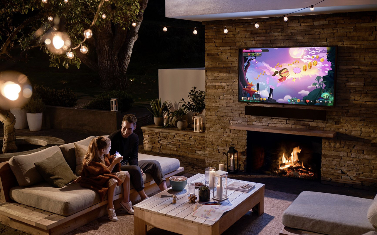 A father and child outside watching TV on a Samsung The Terrace TV.