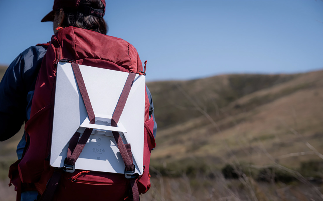 A person walking in a remote area with a Starlink Mini Kit in their backpack.