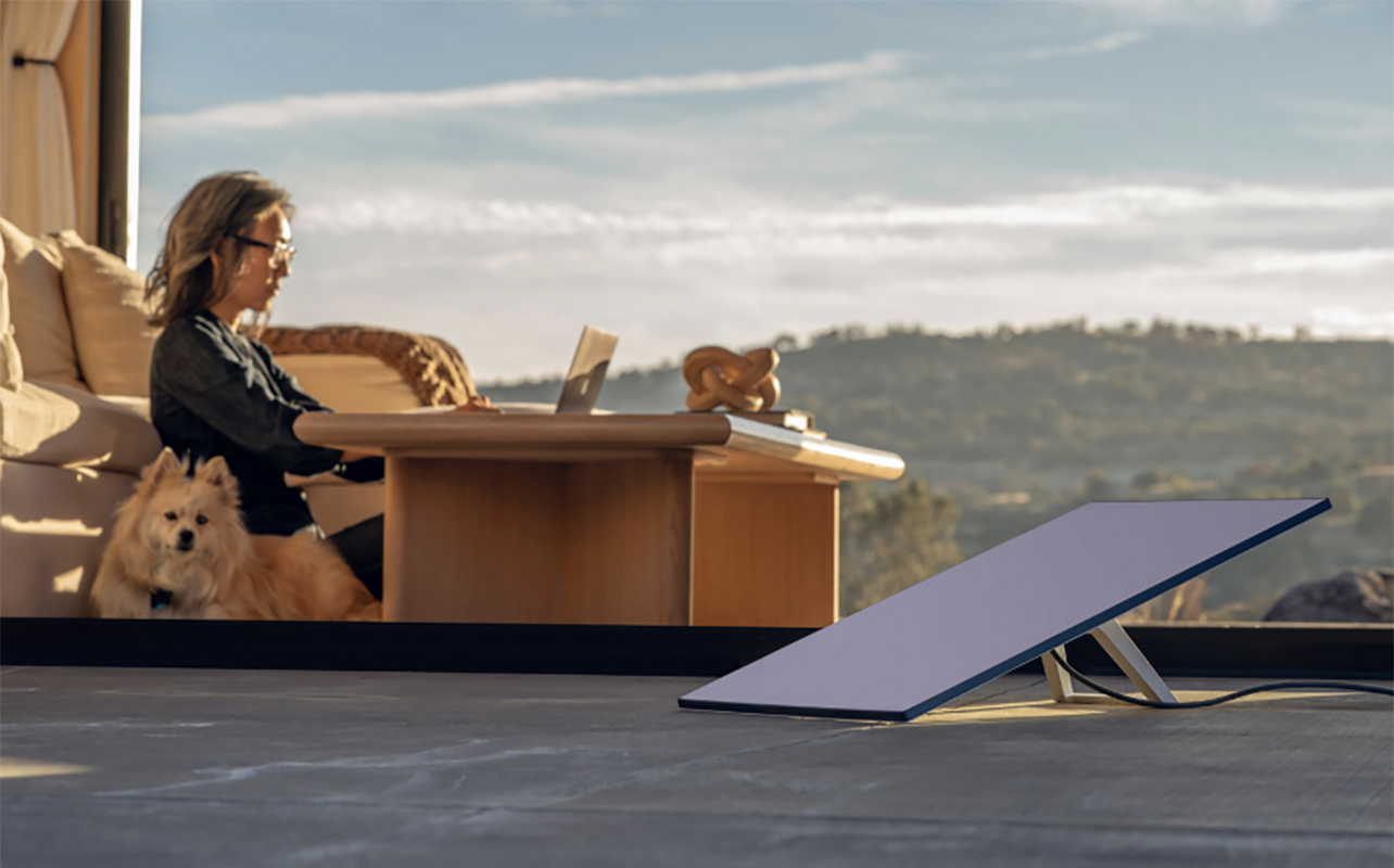 A Starlink Standard Kit on a patio with a person working on a laptop in the background.
