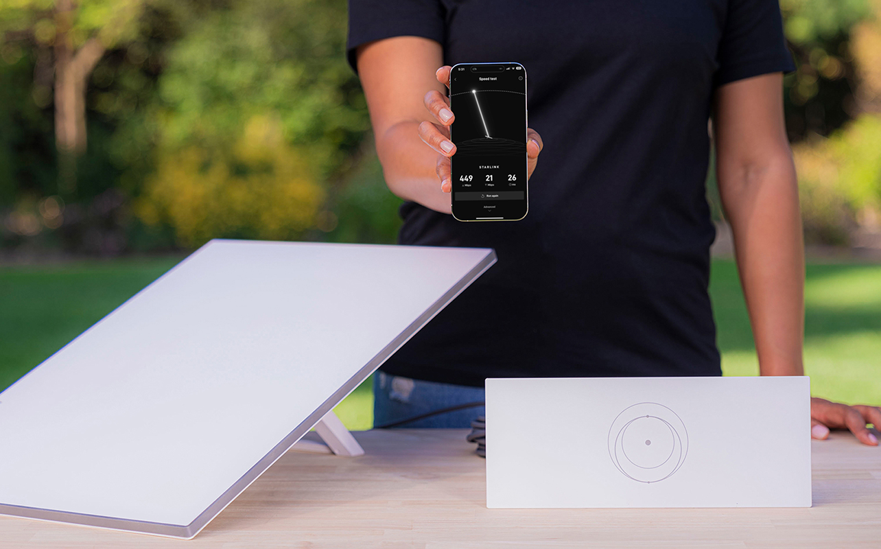 A man holding a phone with the Starlink app alongside Starlink equipment on a table.