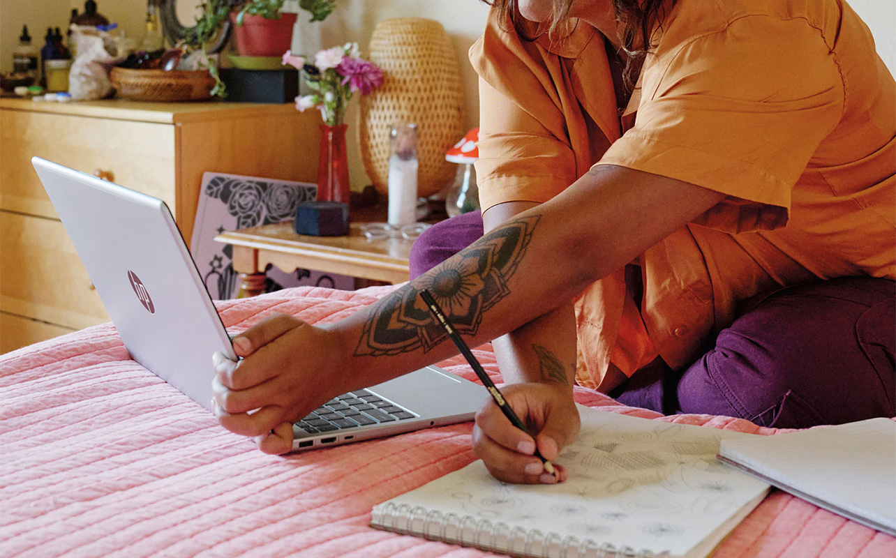 A man looking at his HP laptop and writing notes on a piece of paper.