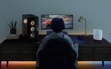 The back of a man playing video games at a computer desk with the Eero Max 7 Wi-Fi mesh system.