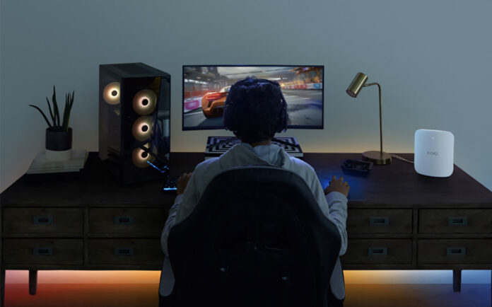 The back of a man playing video games at a computer desk with the Eero Max 7 Wi-Fi mesh system.