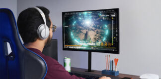 A man sitting at a desk playing games on a computer with an eero Pro 6 mesh Wi-Fi node beside him.