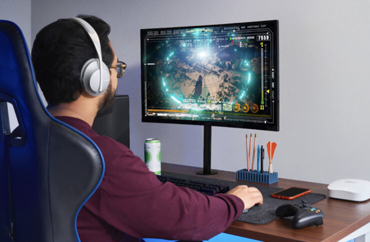 Do you really need the fastest internet speed available? A man sitting at a desk playing games on a computer with an eero Pro 6 mesh Wi-Fi node beside him.