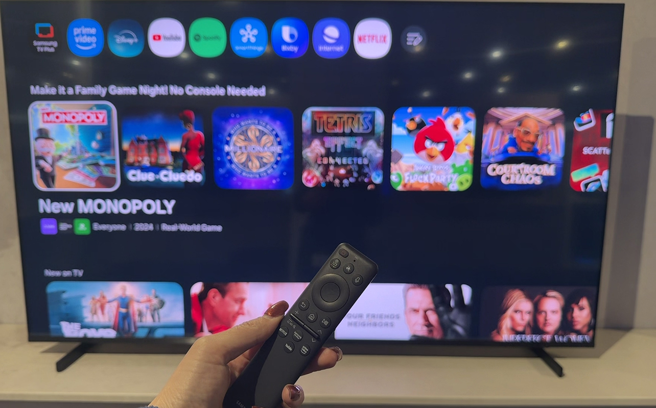 The Samsung R85H Micro RGB TV showing a menu with a hand with the remote in front of it.
